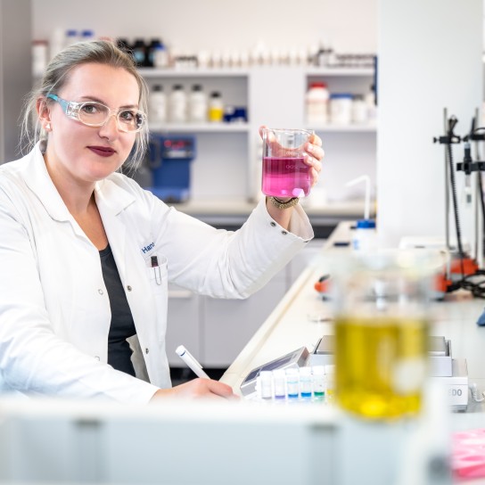 Female chemist holding up a test laboratory bottle in the application kitchen, Essen, Germany