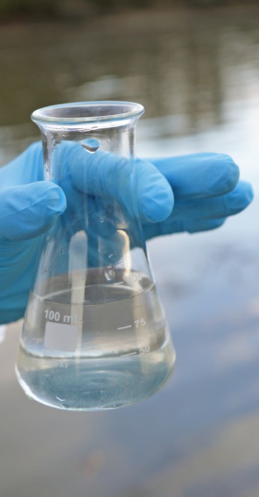 hand with protective clothing holding a flask of water above lake
GettyImages-1337888908.jpg