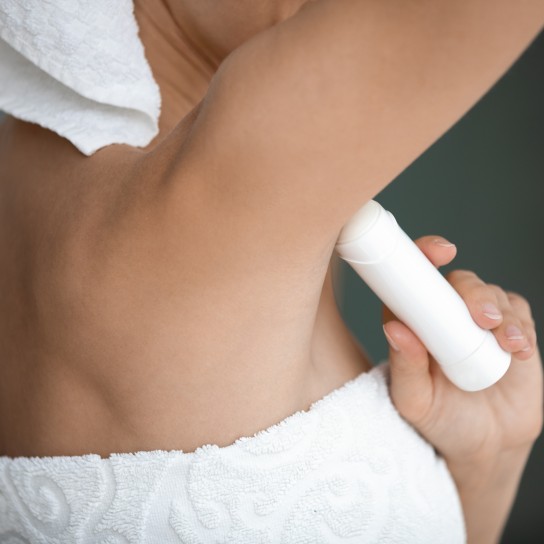 Young lady wrapped in white towel raise arm apply antiperspirant in armpit, woman use underarm deodorant stick for daily hygiene everyday freshness, hyperhidrosis treatment concept close up rear view