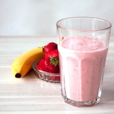 Strawberry milskhake in glass, bowl of strawberries and banana on white vintage wooden background . Soft focus. Copy space. Healthy eating, healthy breakfast concept