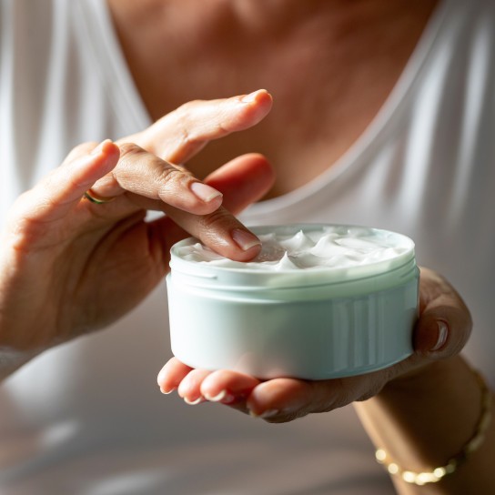 Female hand holding face cream from jar and picking with finger for application