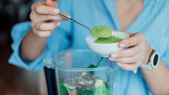 Close up woman adding wheat grass green powder during making smoothie on the kitchen. Superfood supplement. Healthy detox vegan diet. Healthy dieting eating, weight loss program. Selective focus.
