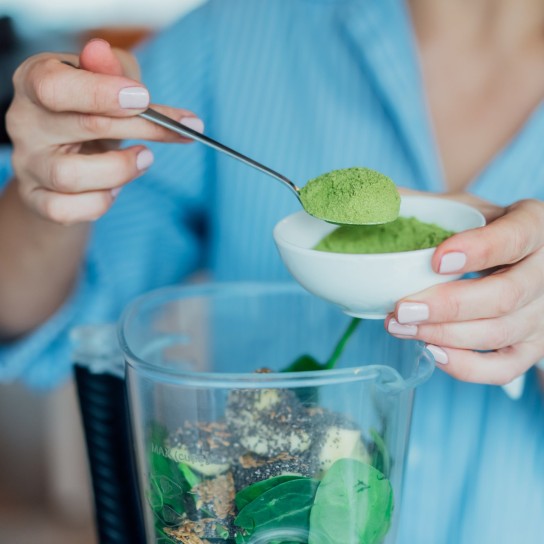 Close up woman adding wheat grass green powder during making smoothie on the kitchen. Superfood supplement. Healthy detox vegan diet. Healthy dieting eating, weight loss program. Selective focus.