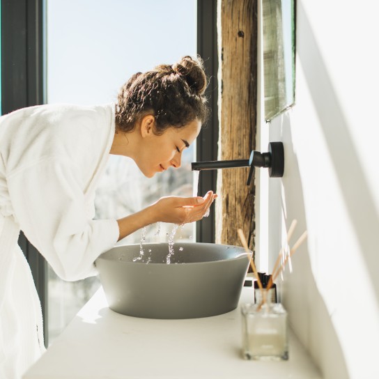 Spa treatment. Bathroom with white walls full of sun light. Black metal furniture. Grey stone sink. Person in bathrobe. Trendy interior design