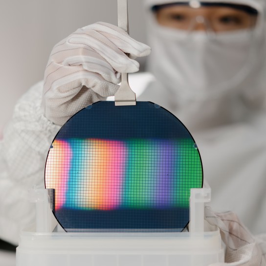 close up of asian male technician in sterile coverall holds wafer that reflects many different colors with gloves