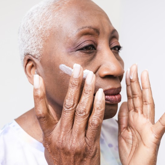 Senior black woman applying face cream to the face