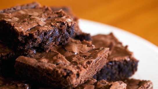 Stůl a na něm talíř chutných nadýchaných čokoládových brownie nakrájených na čtverečky