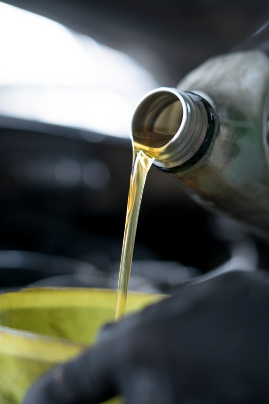 Close up of hand car mechanic refueling and pouring oil fill the oil in the engine, maintenance, and performance in auto repair shop.