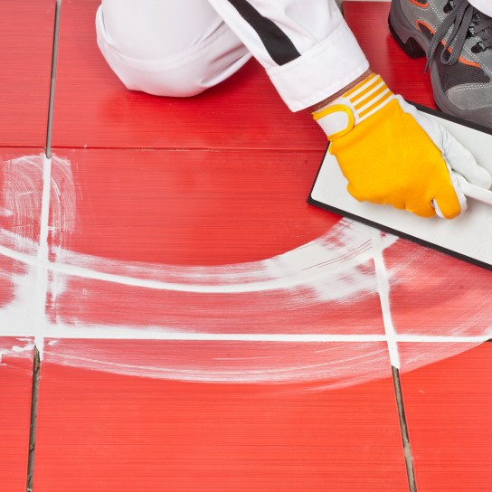 Worker with rubber trowel applying grout tile