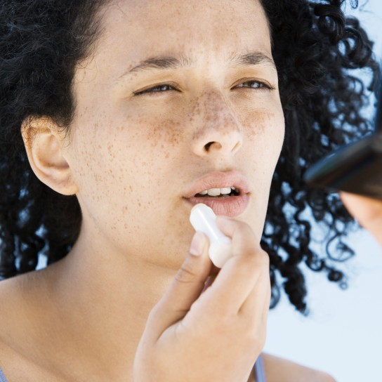 Woman applying lip balm, holding compact