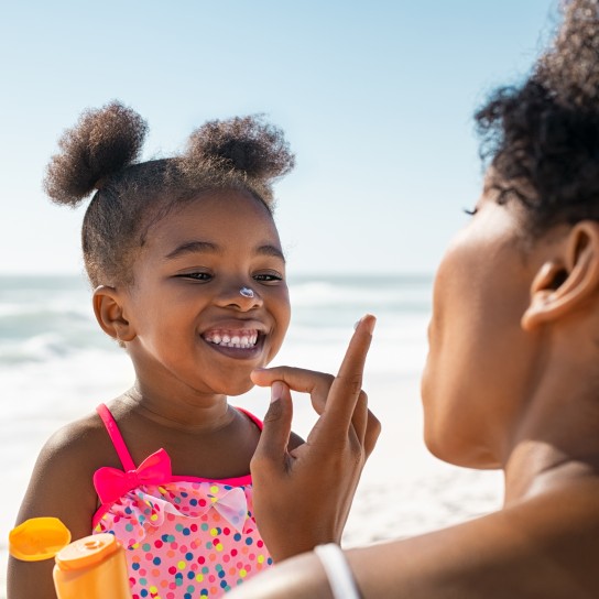Young mother applying protective sunscreen on daughter nose at beach with copy space. Black woman hand putting sun lotion on female child face. African american cute little girl with sunblock cream at seaside.
GettyImages-1369509501.jpg