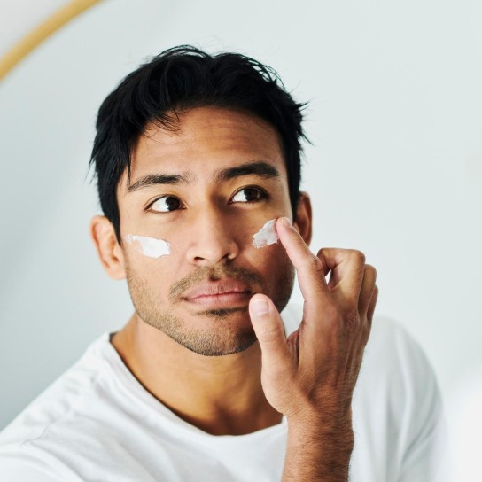 Man applying cream, lotion and moisturizer for a skincare routine while grooming in a mirror at home. Handsome young guy using sunscreen lotion with spf for uv protection on his face for healthy skin
GettyImages-1412486543.jpg