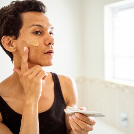 Reflection of handsome person applying cosmetic cream to his face