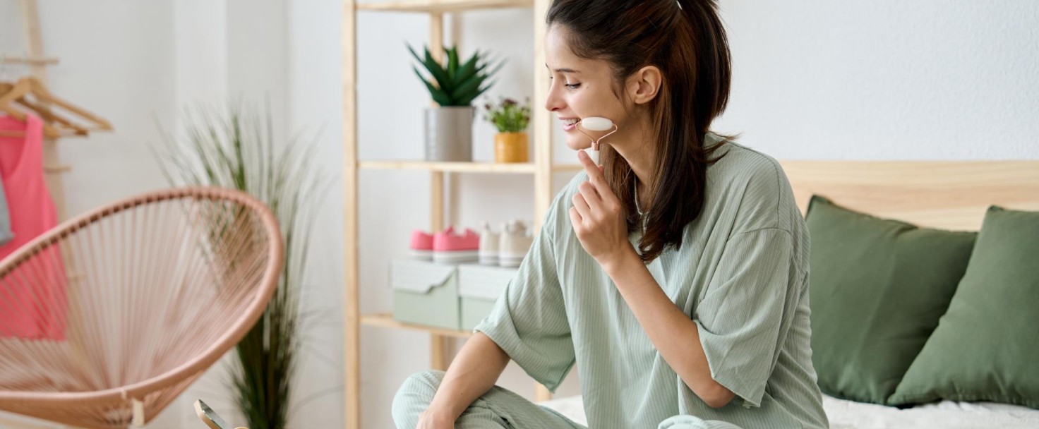side view of a young woman enjoying a jade roller facial massage while sitting up in bed in the morning on her skin care routine.
GettyImages-1498489955.jpg