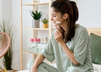side view of a young woman enjoying a jade roller facial massage while sitting up in bed in the morning on her skin care routine.
GettyImages-1498489955.jpg