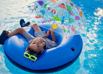 Young boy in swim raft with rubber boots, goggles, and umbrella in pool