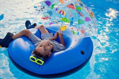 Young boy in swim raft with rubber boots, goggles, and umbrella in pool