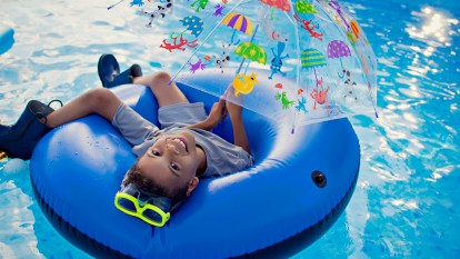 Young boy in swim raft with rubber boots, goggles, and umbrella in pool